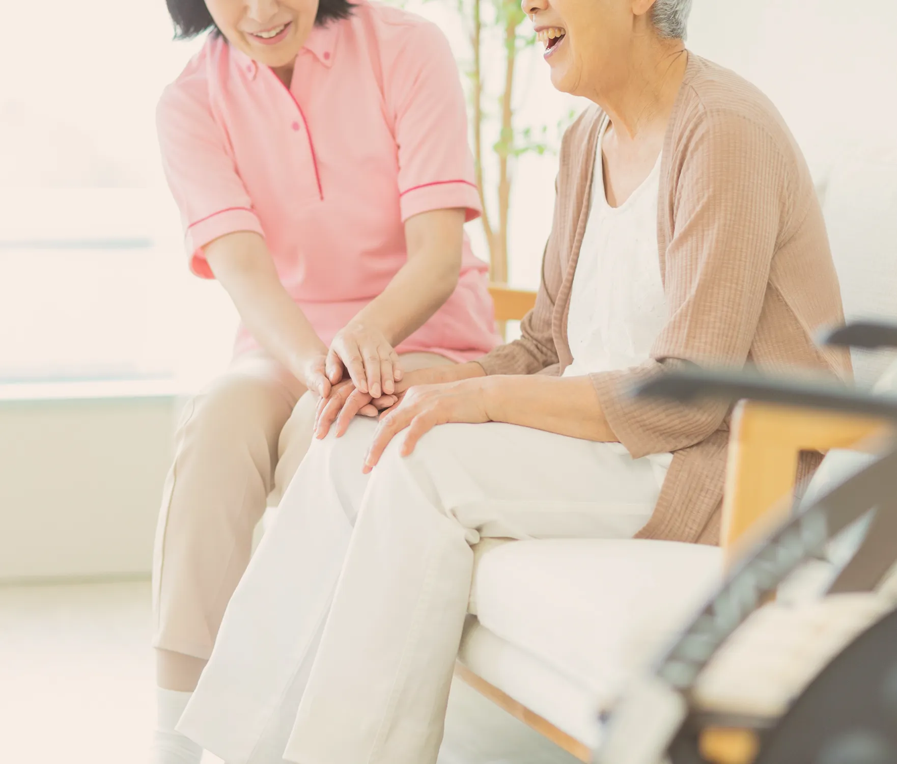 歩行器を使う高齢者の手を、介護士が優しく支えている様子。